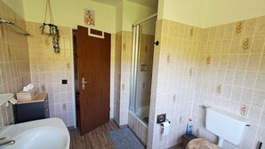 A bathroom with a wooden floor, a white sink, a toilet with a wooden seat, a glass shower enclosure, and a towel rack.