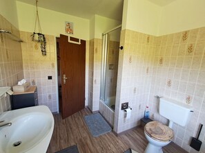 A bathroom with a wooden floor, a white sink, a toilet with a wooden seat, a glass shower enclosure, and a towel rack.