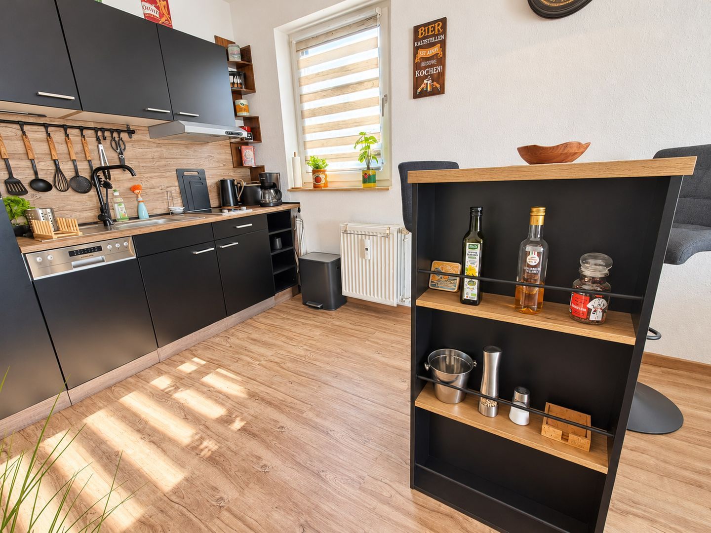 Una cocina moderna con gabinetes negros, encimera de madera y estante empotrado con utensilios de cocina.