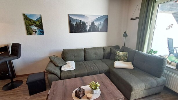 A modern living room with a sectional sofa, a small table with decorative items, and two landscape paintings on the wall.