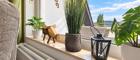 A balcony with potted plants, a wooden sculpture, and a view of the landscape.