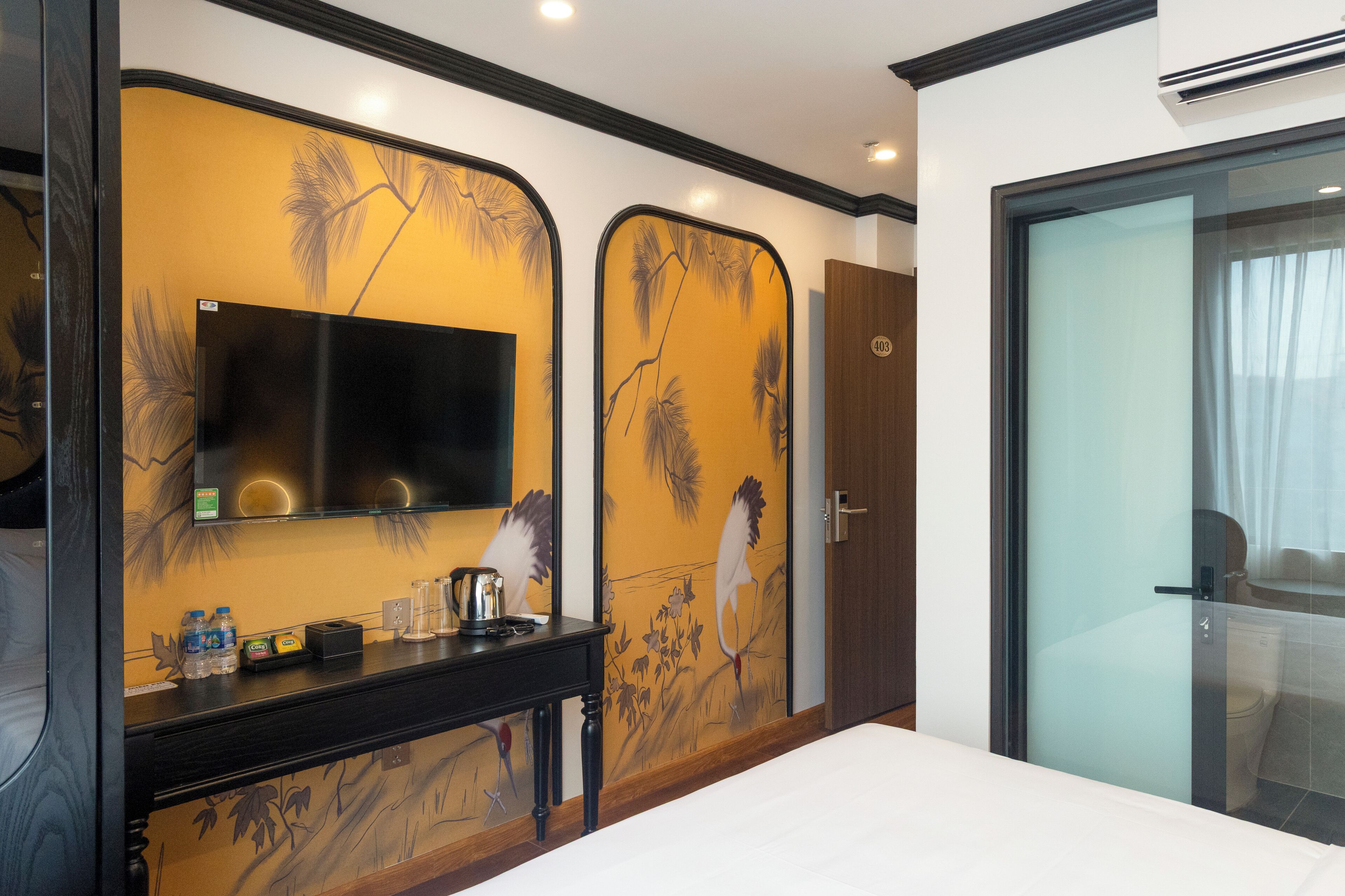 A hotel room with a bed, a vanity with a mirror, a television, and a wall with a nature-themed mural.