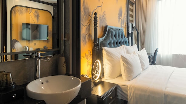 A hotel room with a large bed, a bedside table with a lamp, a bathroom with a sink and mirror, and a TV mounted on the wall. - D'Lux Hotel (Hanoi)