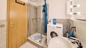 A bathroom with a glass-enclosed shower, a washing machine, and a sink.