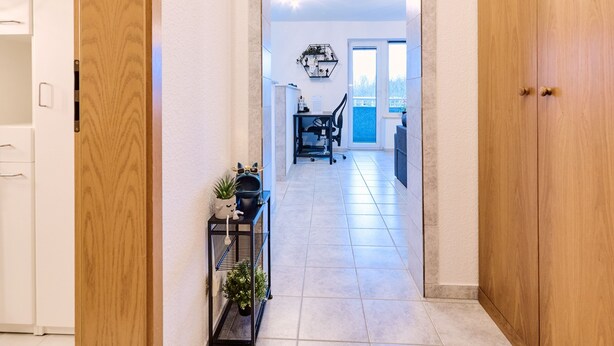 A hallway with wooden doors, a tiled floor, a dining area with a table and chairs, and a view through a glass door.