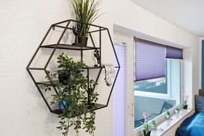 A hexagonal wall-mounted shelf with plants and a clock.
