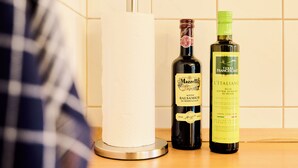 A kitchen counter with a paper towel holder, a bottle of Mazzetti balsamic vinegar, and a bottle of Terre Francescane extra virgin olive oil.