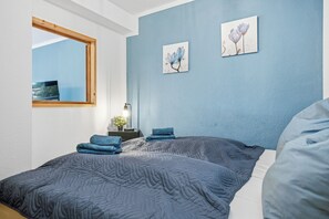 A bedroom with a large bed, a bedside table with a lamp, and two wall-mounted flower paintings. - CASATUA Blue Design - Calm - Workspace - Balcony - Trade Show - WiFi (Wuppertal)