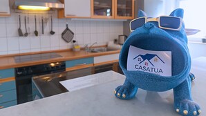 A plush toy with a label in a modern kitchen with wooden cabinets, a stainless steel range hood, and a window.