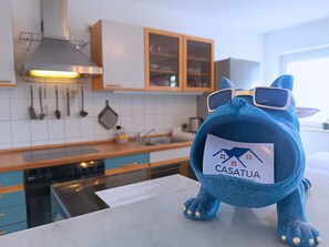 A plush toy with a label in a modern kitchen with wooden cabinets, a stainless steel range hood, and a window.