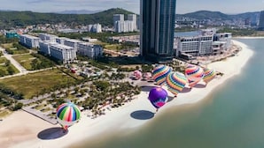 A coastal area with a row of colorful hot air balloons, a beach, and modern buildings in the background. - Sea view Àlacarte Ha Long Bay Apartment (Bai Chay)