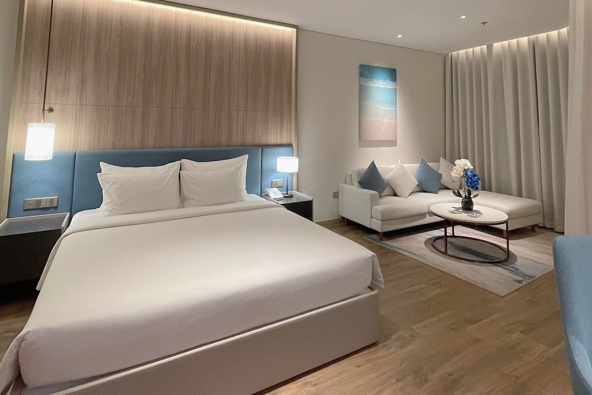 Una habitación de hotel moderna con una cama grande, un sofá, una mesa de centro y un escritorio con lámpara.