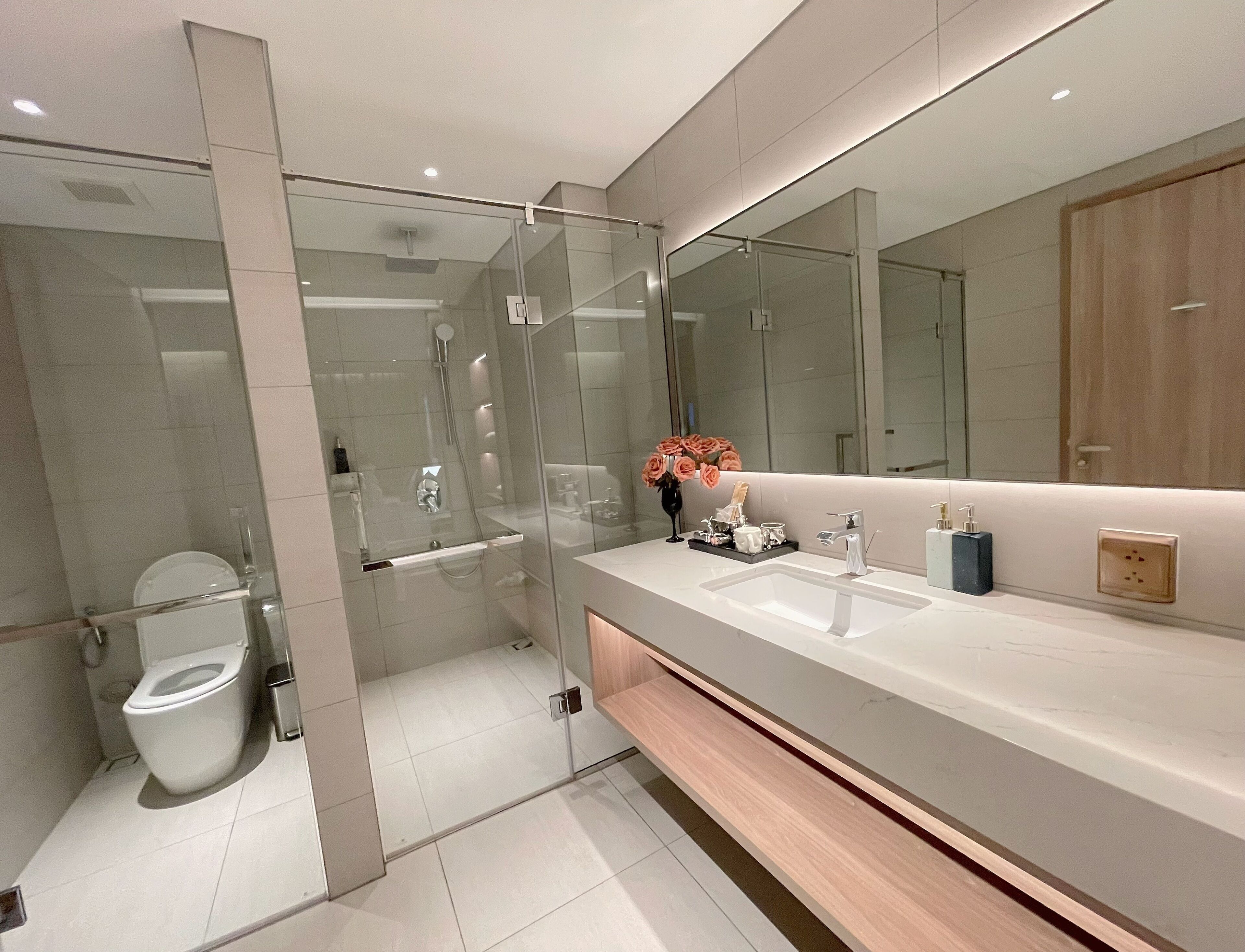 A modern bathroom with a glass-enclosed shower, a white sink, and a large mirror.