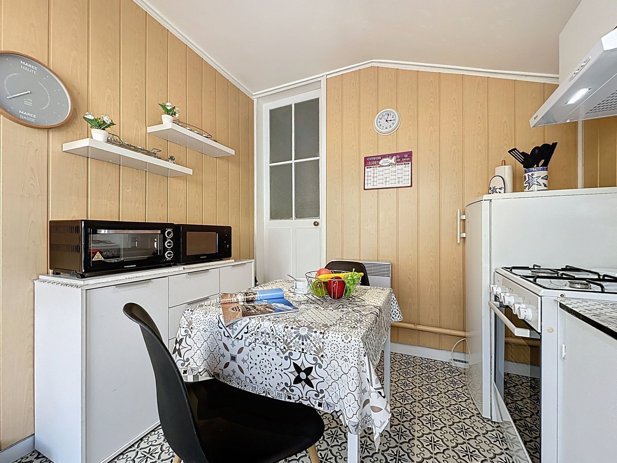 Cocina compacta con microondas, estufa y una mesa con mantel estampado.