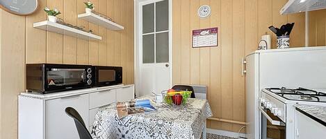 Cocina compacta con microondas, estufa y una mesa con mantel estampado.