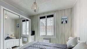 Ein Schlafzimmer mit einem großen Bett, einem Spiegel, einer Chandelieber und einem Fenster mit gemusterten Vorhängen.