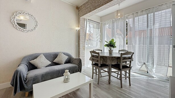 Ein Wohnzimmer mit grauem Sofa, einem weißen Couchtisch und einem Essbereich mit rundem Tisch und Stühlen.
