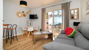Una sala de estar moderna con un sofá gris, una mesa de comedor con sillas, un televisor montado en la pared y un balcón con vistas.
