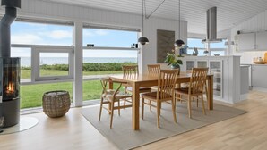 A modern kitchen with white cabinetry, a dining area with wooden furniture, and a large window overlooking a grassy area. - "Gertje" - 20m from the sea by Interhome (Assens)