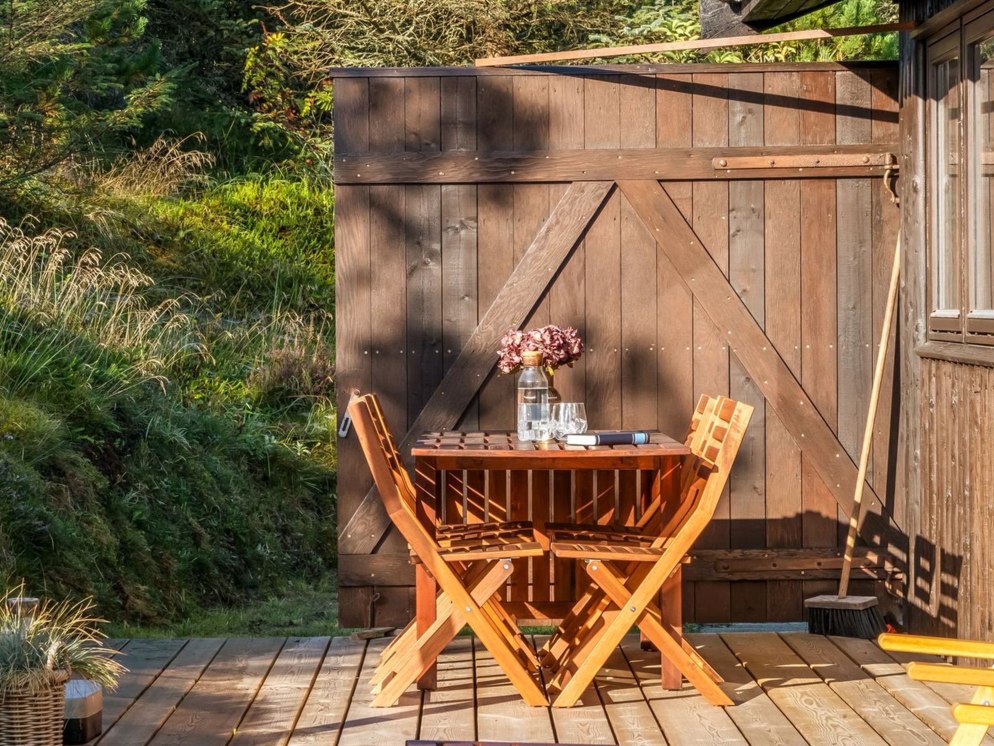 A wooden deck with a table and chairs, a wooden fence, and greenery in the background.