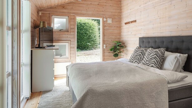 A bedroom with a bed, bedside table, lamp, and a view of a garden.
