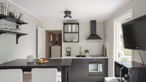 A modern kitchen with a black countertop, white chairs, a built-in oven, and a TV mounted on the wall.