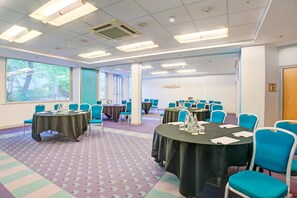 A conference room with multiple tables and chairs, large windows, and a patterned carpet.