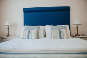 A neatly made bed with a blue headboard, two bedside lamps, and striped pillows. - Atlantic Tower hotel by Sunday Junior Suite (Liverpool)