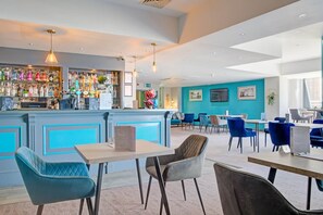 A modern bar area with a variety of liquor bottles, a seating area with blue chairs and tables, and a bright interior with natural light.