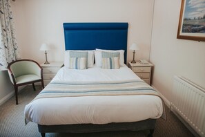 A neatly made bed with a blue headboard, two bedside tables with lamps, a chair, and a painting on the wall. - Atlantic Tower hotel by Sunday Junior Suite (Liverpool)