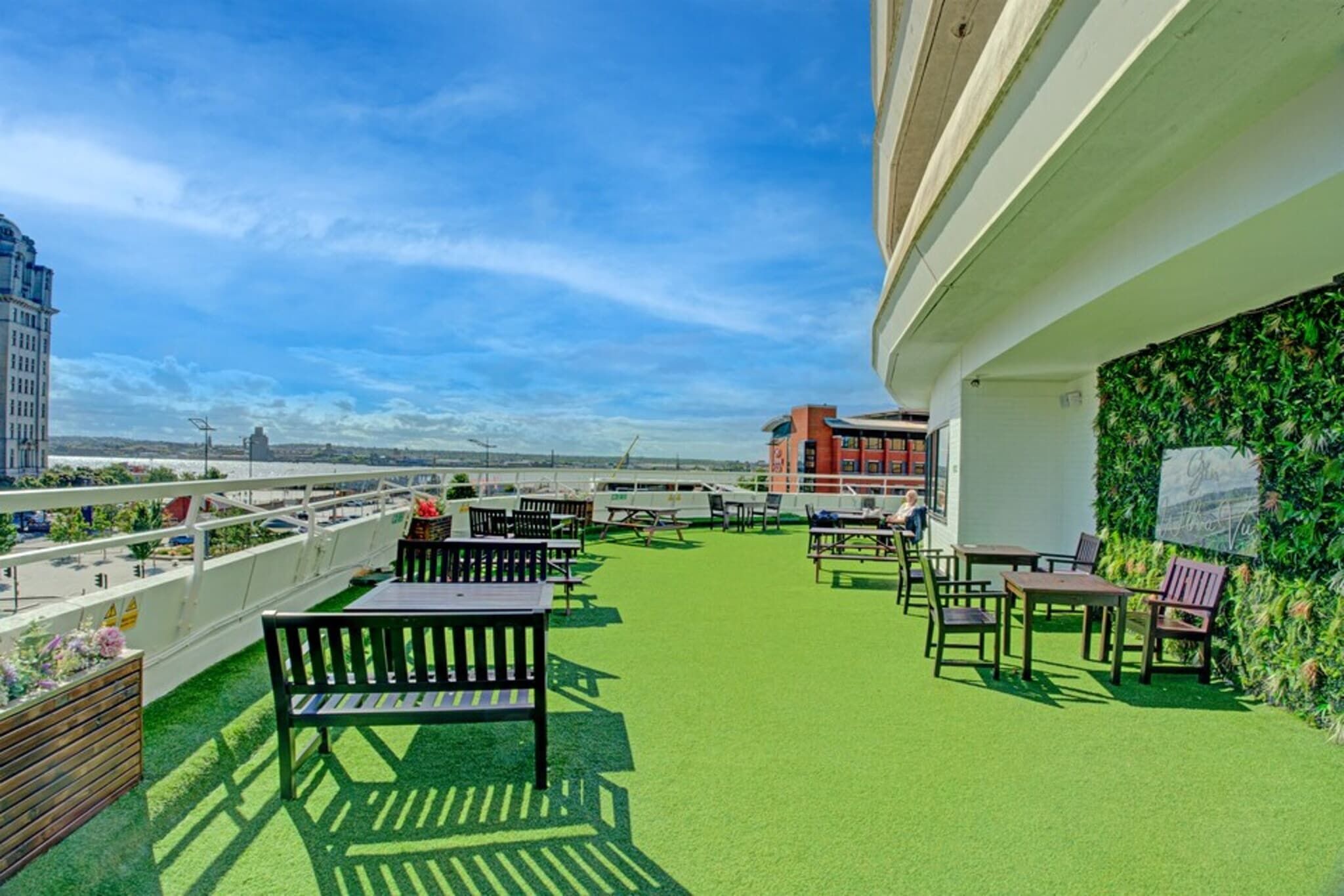 Terraço no telhado com grama sintética verde, área de estar externa e vista do horizonte urbano.