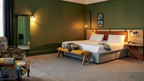 A hotel room with a bed, a bench, a chair, a bedside table, and a mirror.