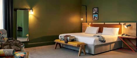 A hotel room with a bed, a bench, a chair, a bedside table, and a mirror.