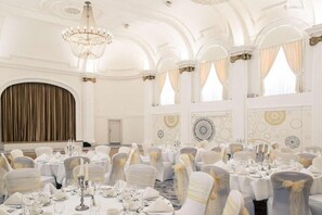 A banquet hall with round tables, white chairs, chandeliers, and decorative wall patterns. - Bristol Grand Hotel By Sunday - Junior Suite (Bristol)
