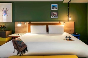 Habitación de hotel ordenada con una cama grande, una mesita de noche con lámpara y obras de arte en las paredes.