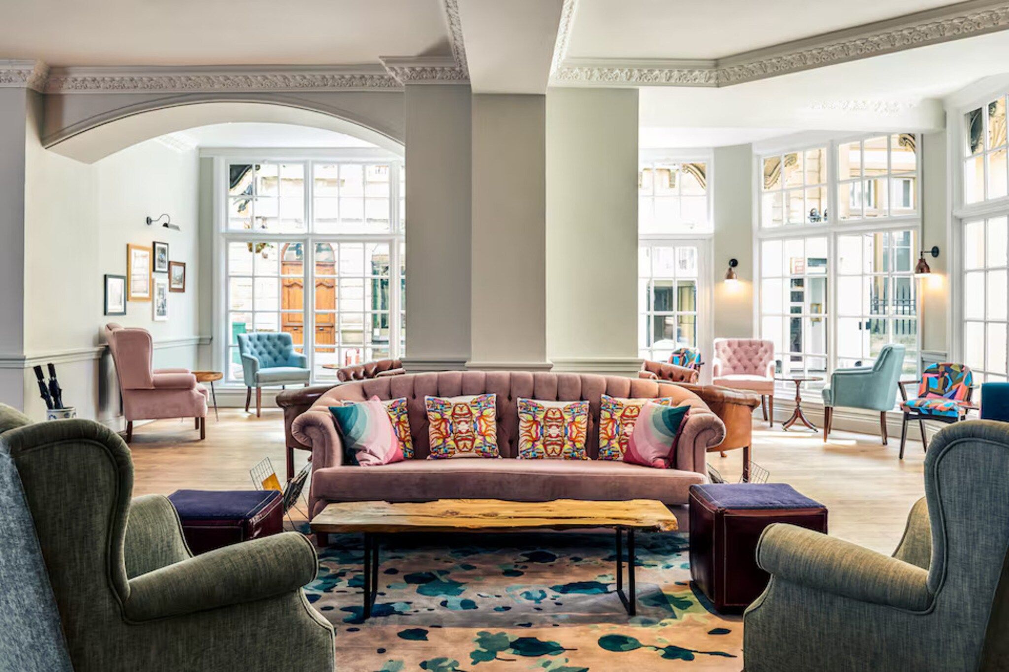 A spacious lounge area with a large, plush sofa adorned with colorful pillows, surrounded by various seating options and a patterned rug.