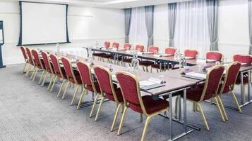 A conference room with a long table, red chairs, and a projector screen.