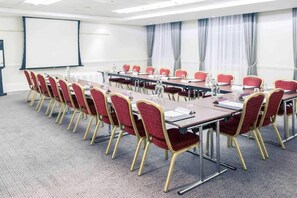 Un salón de conferencias con una larga mesa, sillas rojas y una pantalla de proyector.