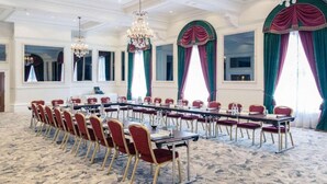 A conference room with a long table, red chairs, and chandeliers.