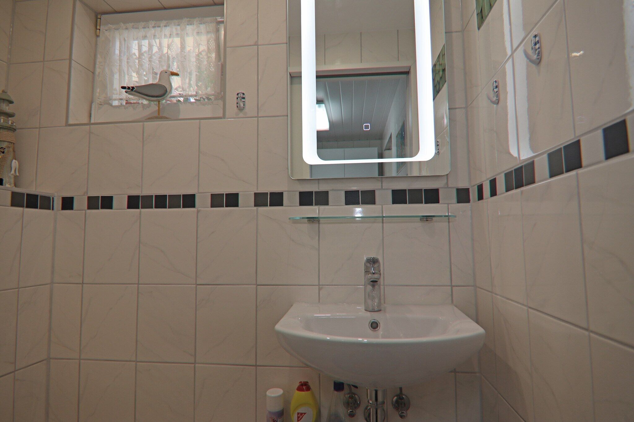 Une salle de bain avec un lavabo blanc, un miroir et une petite fenêtre avec un rideau.