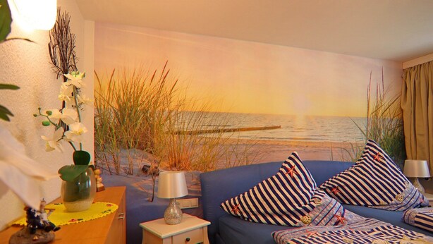 Een kamer met een bed, nachtkastje, lamp en een muurschildering van een strand.