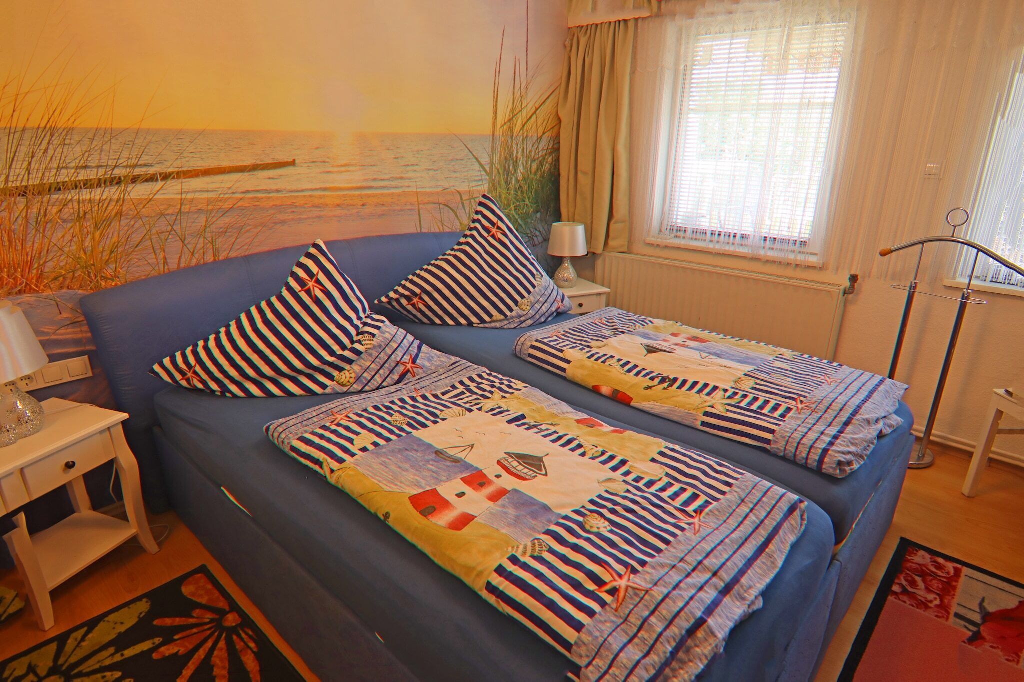 A bedroom with a bed covered in striped bedding, a nightstand with a lamp, and a window with curtains.