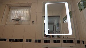Een badkamer met een grote spiegel, een raam met gordijn en een glazen plank.