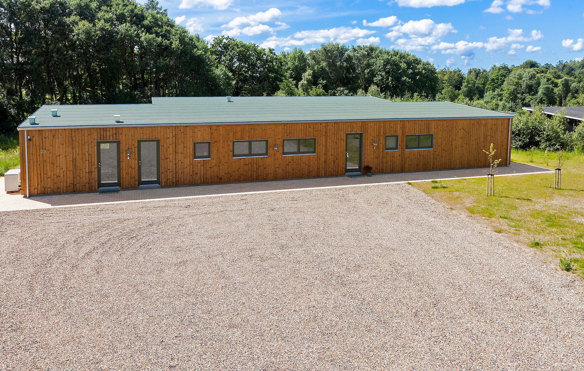 A modern building with a green roof, wooden exterior, and a gravel driveway.