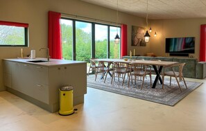 Une cuisine moderne avec un îlot central, un coin repas avec des chaises, un canapé et un téléviseur dans le salon.