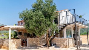 A stone-walled building with a staircase leading to a balcony, surrounded by a garden and a view of the countryside. - Natur Olive House Ston (Ston)