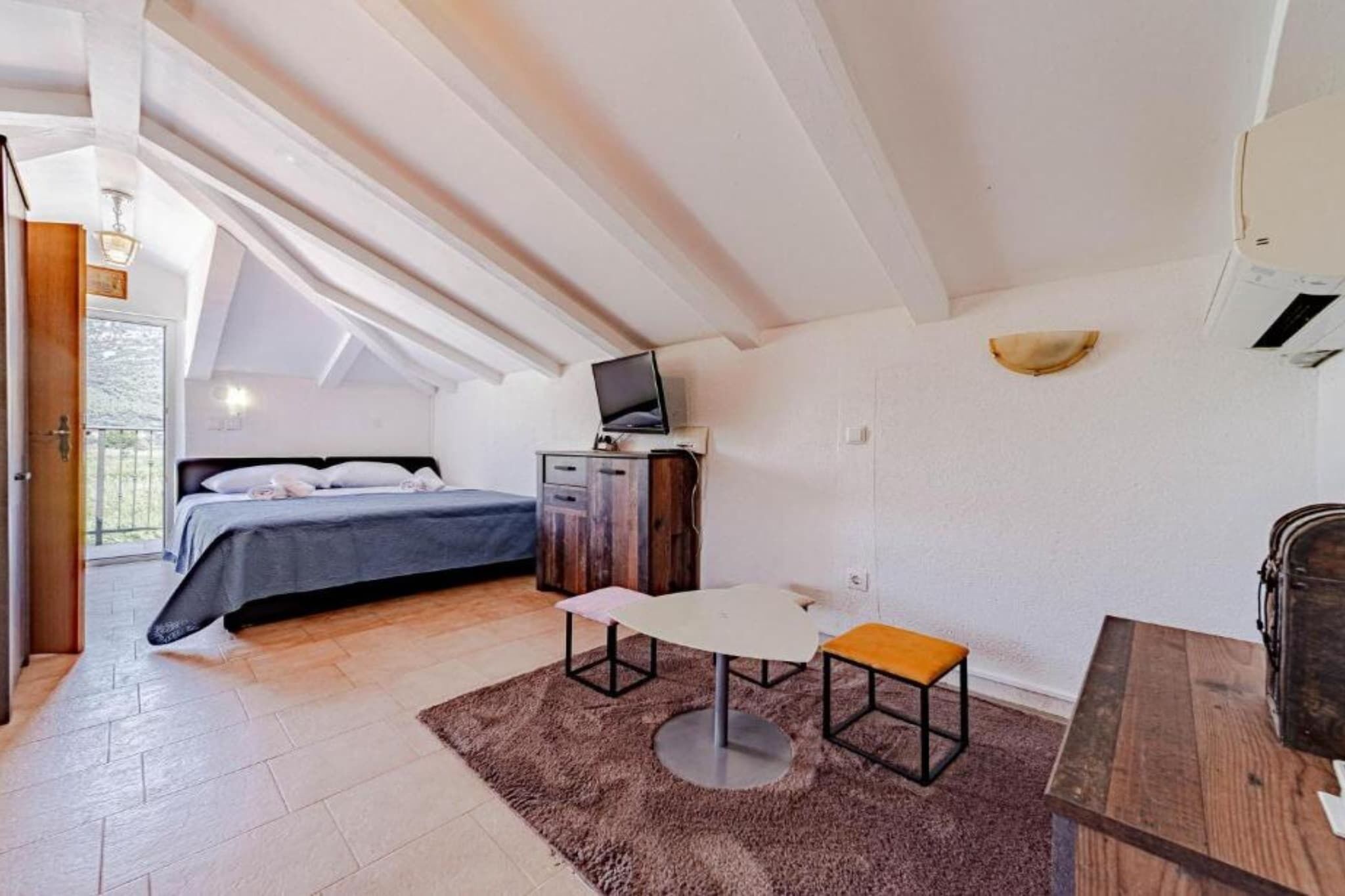 A bedroom with a bed, a desk, a chair, a television, and a window.