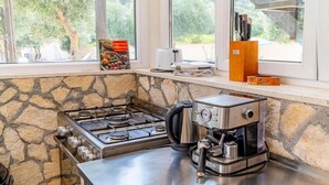 A kitchen with a gas stove, coffee maker, and a view of the outdoors through large windows. - Natur Olive House Ston (Ston)