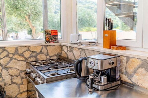 Una cocina con estufa a gas, cafetera y vistas al exterior a través de amplios ventanales.