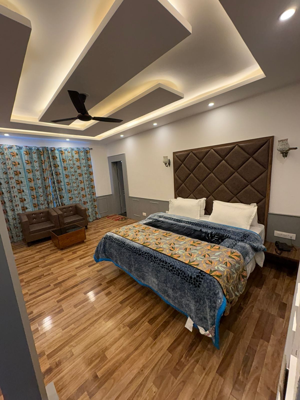 A modern bedroom with a large bed, a ceiling fan, and a wooden floor.